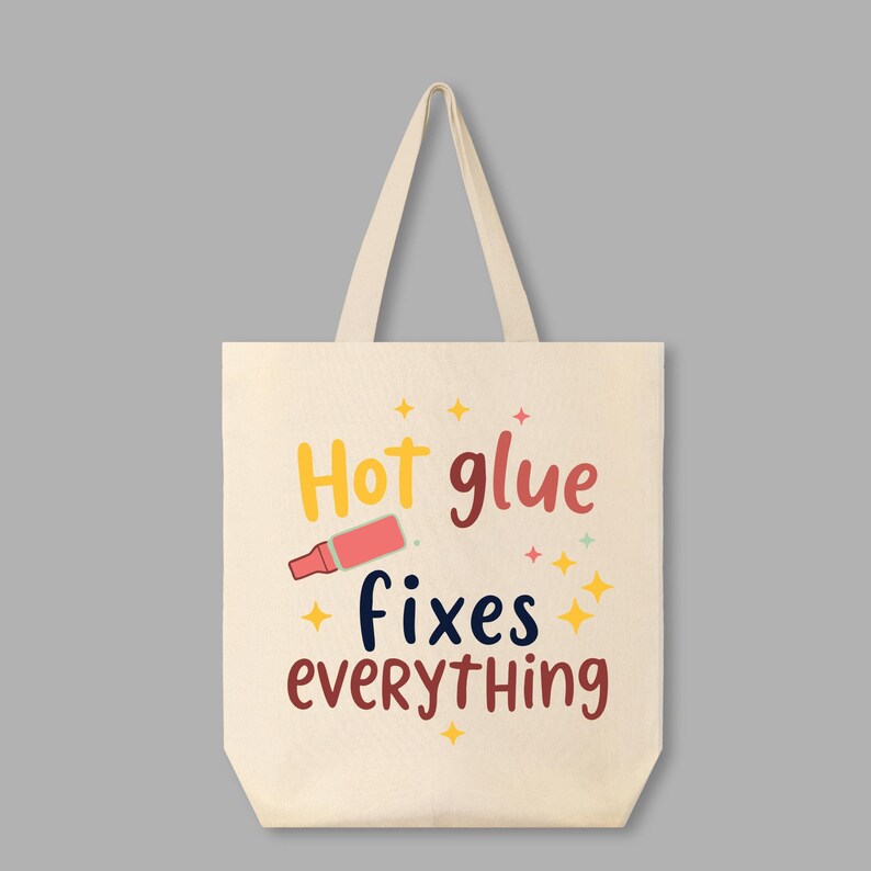 May include: A white canvas tote bag with the text "Hot glue fixes everything" in colorful letters. A pink hot glue gun is pictured next to the text.