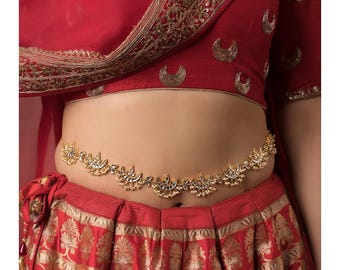 May include: A gold waist belt with a crescent moon design and pearl accents. The belt is worn over a red skirt with a floral pattern.