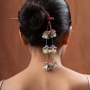 May include: A wooden hair stick with dangling silver bells and colorful beads. The stick is inserted into a woman's hair bun.