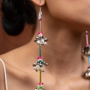May include: Long silver dangle earrings with multiple tiers of small bells and colorful beads. The earrings are suspended from a silver hook.