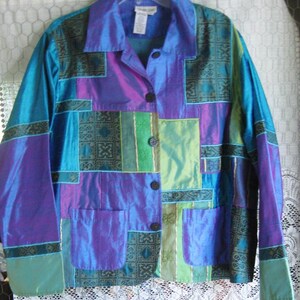 May include: A long-sleeve button-down jacket featuring a patchwork design in iridescent shades of blue, purple, and green. The garment includes two front patch pockets, a standard collar, and dark circular buttons down the center front closure.