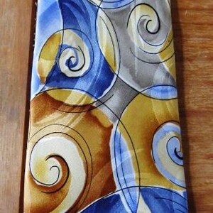 May include: A necktie featuring a repeating abstract pattern of swirling circular shapes in shades of golden yellow, deep blue, light blue, and grey. The design consists of overlapping spirals and curved lines that create a fluid, continuous visual effect across the entire length of the fabric surface.