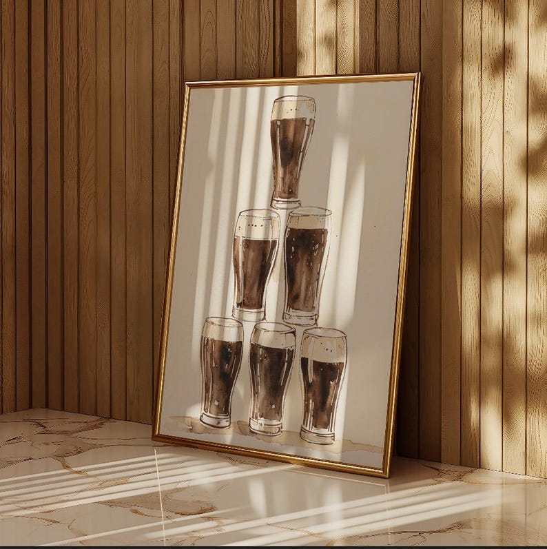 May include: A framed print featuring a watercolor illustration of six beer glasses arranged in a pyramid. The glasses are filled with dark beer, and the artwork has a gold frame. The background is a neutral white.