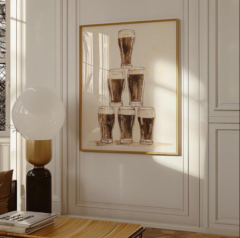 May include: A framed print featuring a watercolor illustration of seven pint glasses filled with dark beer. The glasses are arranged in a pyramid shape against a neutral background, with a gold-colored frame. The artwork is displayed on a white wall.