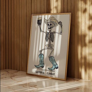 May include: A framed print featuring a skeleton cowboy holding a pint of Guinness. The skeleton wears a cowboy hat and boots. The text "Guinness Cowboy" is at the bottom of the print. The frame is gold.