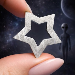 May include: A silver-toned star-shaped object with a hollow center and a distinct, etched cross-hatched surface texture. The metallic star features sharp, defined points and a flat, geometric design, showcasing a unique pattern across its entire surface.