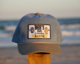May include: A light blue denim baseball cap with a brown brim and a patch that reads "DEE'S Nuts & Candies Best in Town". The patch features a cartoon peanut and a can of nuts.
