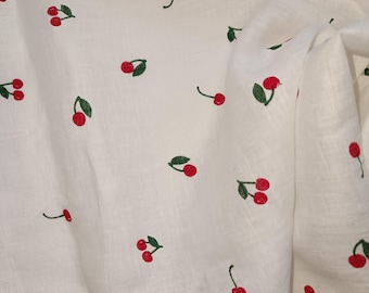 May include: White fabric with a repeating pattern of red cherries with green stems and leaves.