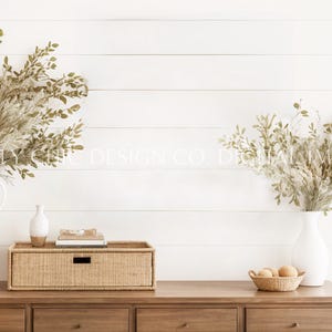 Może przedstawiać: Biała drewniana komoda z czterema szufladami, wiklinowym koszem do przechowywania i dwoma białymi wazami z suszoną trawą pampasową i zielenią. Komoda stoi przy białej ścianie z desek.