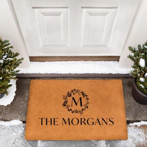 May include: A brown coir doormat with the text "The Morgans" and a wreath with the letter "M" in the center.