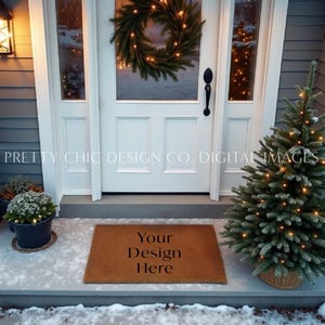 May include: A brown doormat with the text "Your Design Here" on it. The doormat is in front of a white door with a Christmas wreath on it. There is a small Christmas tree with lights on it to the right of the doormat.