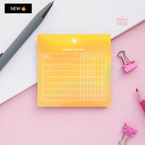 Pode incluir: Um bloco de notas adesivas amarelo para o acompanhamento de hábitos com um gráfico de sol e o texto "habit tracker" no topo. A nota está dividida em colunas etiquetadas como "habit" e "sun, mon, tue, wed, thu, fri, sat".