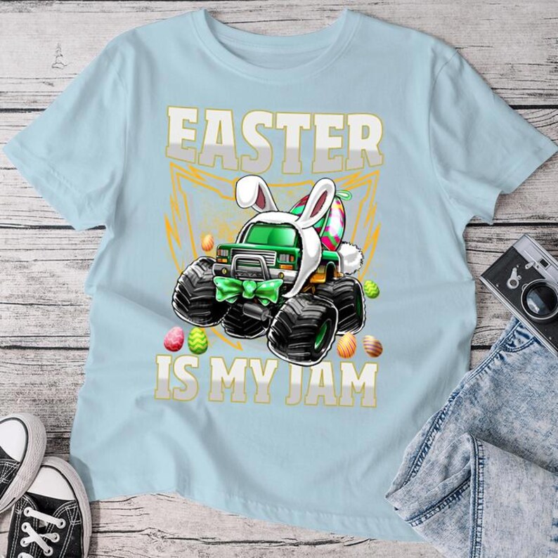 May include: Light blue t-shirt with a green monster truck wearing bunny ears and holding Easter eggs. The text "Easter is my jam" is printed on the shirt.