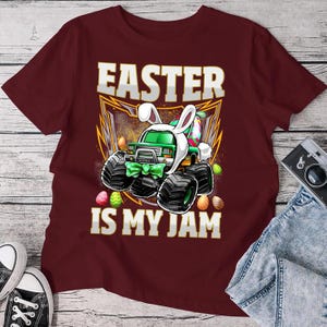 May include: A maroon t-shirt with a green monster truck wearing bunny ears and holding Easter eggs. The text "Easter is my jam" is printed on the shirt.