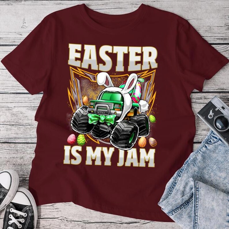May include: A maroon t-shirt with a green monster truck wearing bunny ears and holding Easter eggs. The text "Easter is my jam" is printed on the shirt.