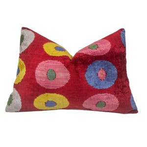 Pode incluir: Travesseiro de veludo vermelho com um padrão geométrico colorido de círculos em tons de rosa, azul, amarelo e verde.