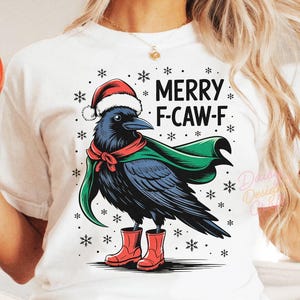 Könnte beinhalten: Weißes T-Shirt mit einem Cartoon-Raben, der einen Weihnachtsmannhut, einen grünen Umhang und rote Stiefel trägt. Der Text "MERRY F-CAW-F" steht über dem Raben. Schneeflocken-Grafiken umgeben den Raben. Der untere Teil des Bildes lautet "DIGITALER DOWNLOAD - PNG-DATEI - 300 DPI".