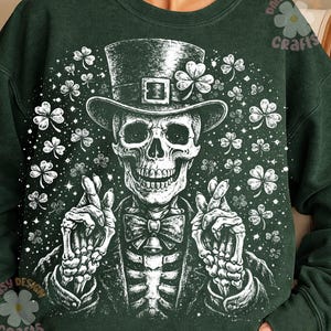 Op de afbeelding: Donkergroene sweatshirt met een witte illustratie van een skelet met een hoge hoed versierd met een klavertje vier. Het skelet draagt een pak en een vlinderdas, omringd door klavers en sterren. Het sweatshirt heeft de tekst "Daisy Design Crafts".