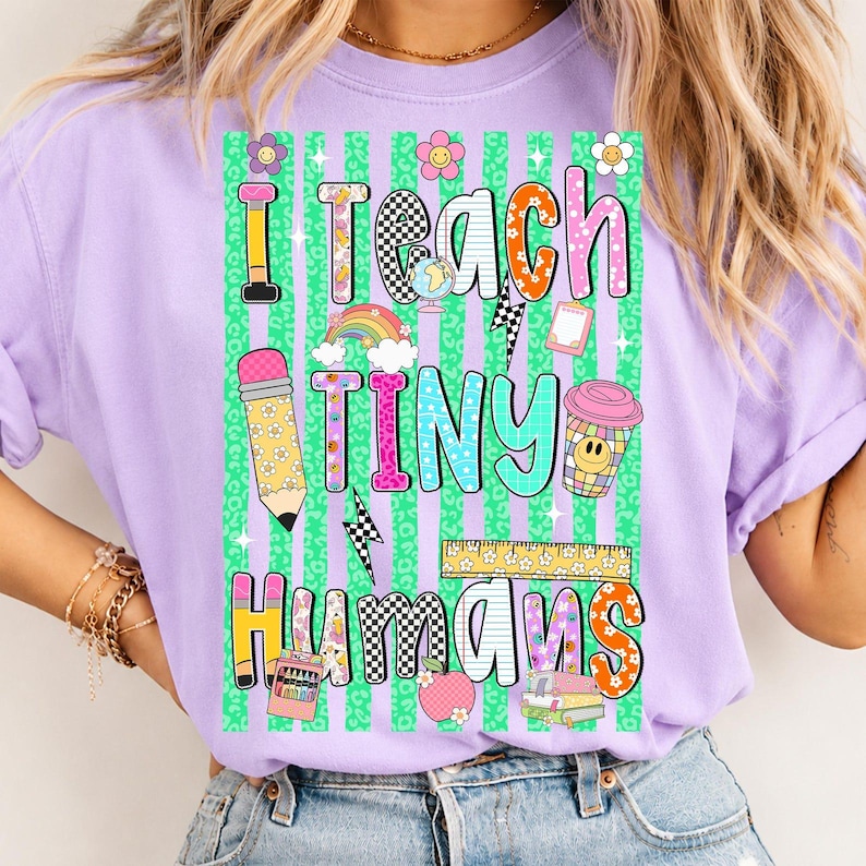 Puede incluir: Una camiseta de color morado claro con un estampado gr&aacute;fico que incluye el texto I TEACH TINY HUMANS. El dise&ntilde;o presenta un fondo de estampado de leopardo verde con rayas verticales, un l&aacute;piz, un globo terr&aacute;queo, un arco&iacute;ris, una taza, una regla y libros.