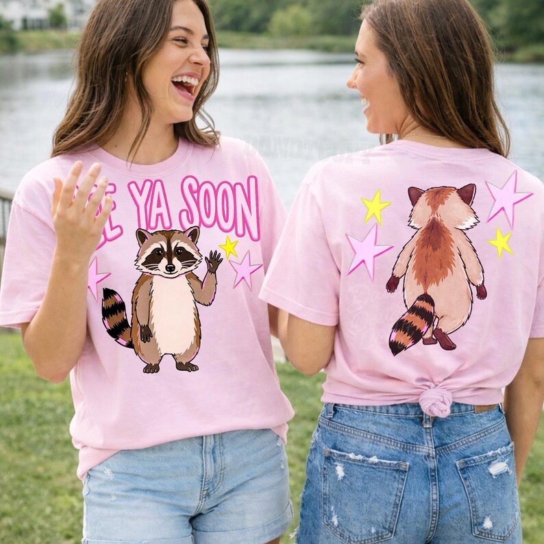 K&ouml;nnte beinhalten: Zwei Frauen tragen hellrosa T-Shirts mit einem Waschb&auml;r-Motiv. Auf der Vorderseite des Shirts steht "See Ya Soon" mit einem winkenden Waschb&auml;ren. Auf der R&uuml;ckseite des Shirts befinden sich Waschb&auml;r- und Sterngrafiken.