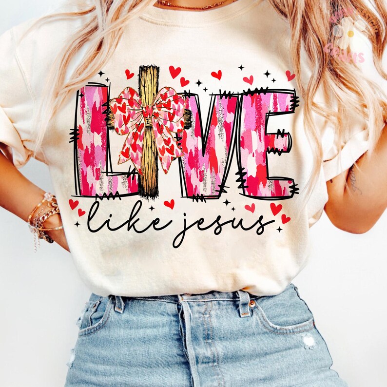 May include: Cream-colored t-shirt with the words "LIVE" in pink and red brushstrokes, a wooden cross, and a bow made of hearts. The phrase "like jesus" is written in cursive below, with red heart accents.