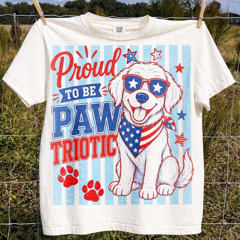 May include: Off-white t-shirt with a patriotic design. The shirt features a cartoon dog wearing sunglasses and a bandana, with the text "Proud to be Paw Triotic" in red and blue. Red paw prints and stars complete the design.
