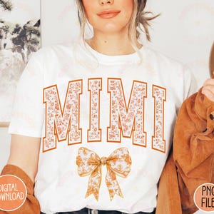 May include: White t-shirt with the word "MIMI" in orange and white floral print. A large orange and white floral bow is below the text.