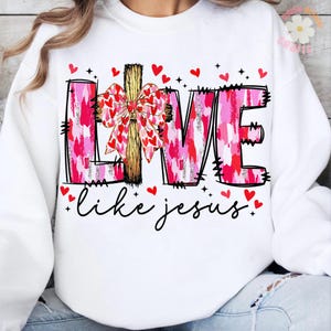May include: White sweatshirt with the word "LIVE" in pink and red brushstroke letters, a wooden cross, and a bow made of hearts. The phrase "like jesus" is written in cursive below, with red hearts scattered around.