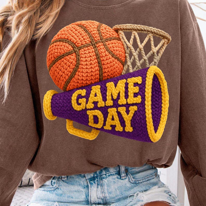K&ouml;nnte beinhalten: Braunes Sweatshirt mit Basketball-, Netz- und Megaphon-Grafik. Das Megaphon ist lila mit gelben Verzierungen und dem Schriftzug "GAME DAY". Der Basketball ist orange und braun.