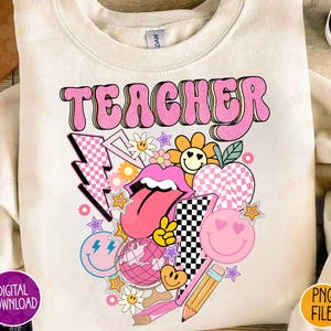 May include: Cream-colored sweatshirt with a retro-style graphic that says "TEACHER" in pink bubble letters. The graphic includes a variety of colorful elements like a smiley face, lightning bolts, and a checkerboard heart.