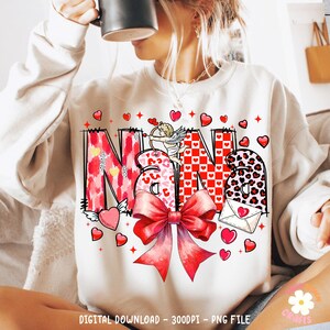 May include: A white sweatshirt with a red, pink, and black graphic design that says "Nana" with a cupid and a bow. The design is surrounded by red hearts.