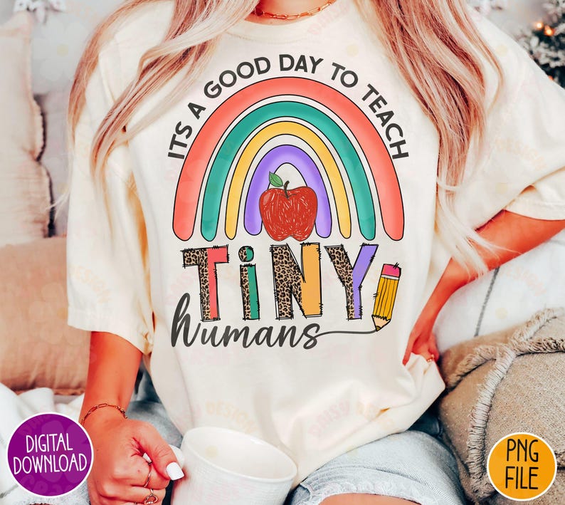 K&ouml;nnte beinhalten: Ein wei&szlig;es T-Shirt mit einem Regenbogen-Design und dem Text "Es ist ein guter Tag, um kleine Menschen zu unterrichten". Der Regenbogen hat einen roten Apfel in der Mitte.