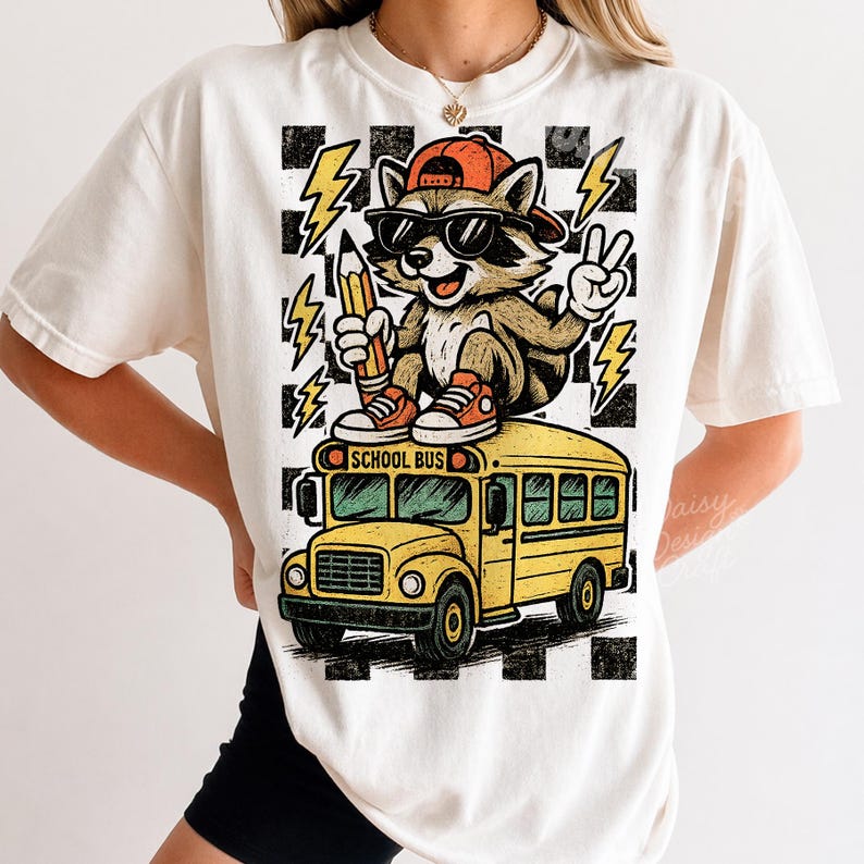 Puede incluir: Una camiseta blanca con un gr&aacute;fico de un mapache con gafas de sol y una gorra naranja, sosteniendo un l&aacute;piz y haciendo el signo de la paz. El mapache est&aacute; sentado sobre un autob&uacute;s escolar amarillo, sobre un fondo de cuadros negros y blancos.