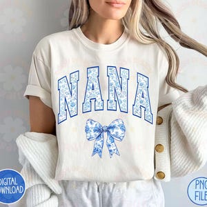 May include: A white t-shirt with a blue and white floral print design that says "NANA" in blue letters with a blue and white floral bow underneath.