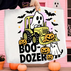 Op de afbeelding: Witte Halloween-draagtas met een spook dat een gele bulldozer bestuurt, pompoenen, zwarte vleermuizen en sterren. De tekst "BOO-DOZER" is in het zwart gedrukt. Een leuk en griezelig ontwerp.