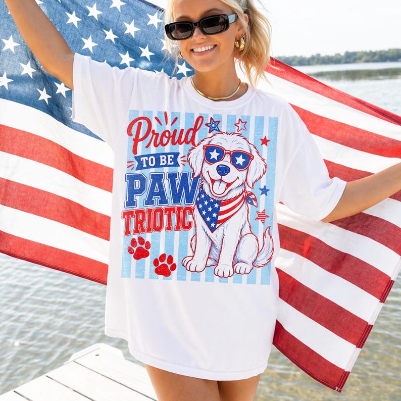 May include: White t-shirt with a patriotic dog graphic. The design features a cartoon dog wearing sunglasses and a bandana, with the text "Proud to be Paw Triotic." The shirt is paired with an American flag.