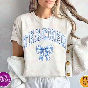 K&ouml;nnte beinhalten: Ein wei&szlig;es T-Shirt mit dem Wort "TEACHER" in blauen Buchstaben und einer blauen und wei&szlig;en Schleife mit einem Blumenmuster.