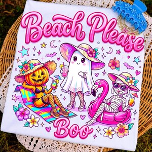 May include: A white t-shirt featuring a colorful graphic with the text Beach Please and Boo. The design includes a pumpkin character, a ghost, and a mummy wearing sun hats and sunglasses, surrounded by tropical flowers, stars, and bats.