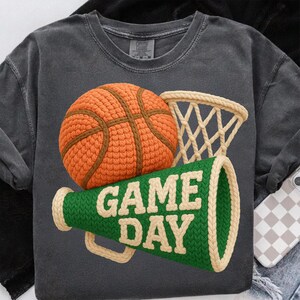K&ouml;nnte beinhalten: Dunkelgraues T-Shirt mit Basketball-, Netz- und Megaphon-Design. Der orangefarbene Basketball hat braune Linien, das Netz ist beige und das gr&uuml;ne Megaphon tr&auml;gt die Aufschrift "GAME DAY" in wei&szlig;en Buchstaben. Ein lustiges, sportliches Thema.