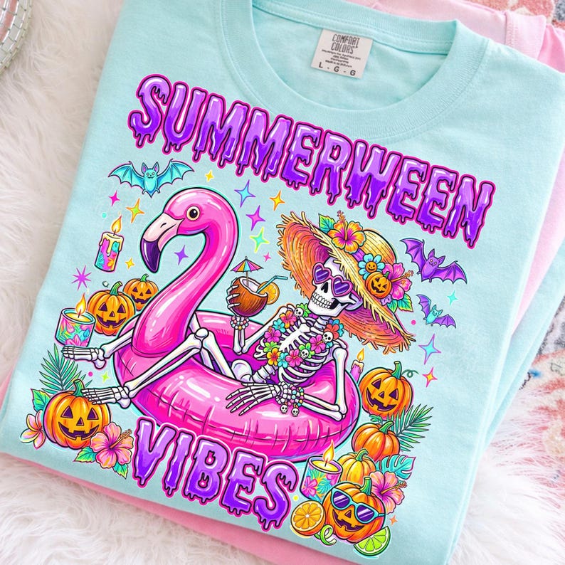 May include: A light blue t-shirt featuring a graphic of a skeleton wearing a straw hat and heart-shaped sunglasses, lounging in a pink flamingo pool float. The design includes pumpkins, bats, tropical flowers, and the text Summerween Vibes.