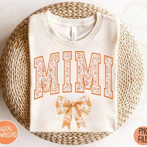 May include: A white t-shirt with the word "MIMI" printed in orange and white floral letters. A small orange and white floral bow is below the word.