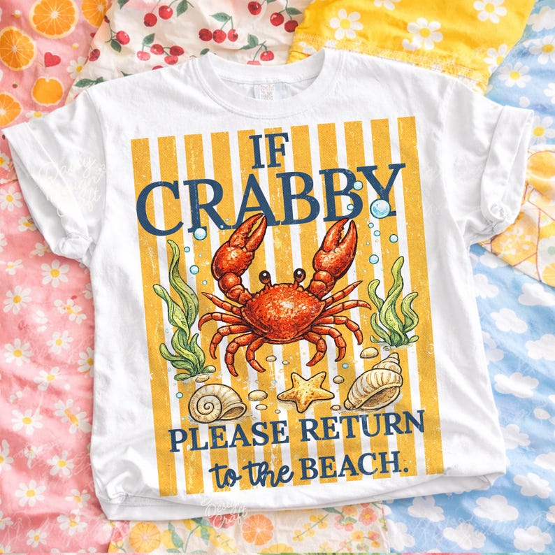 May include: White t-shirt with a colorful crab graphic. The design features a red crab, seaweed, seashells, and the text "IF CRABBY PLEASE RETURN to the BEACH" on a yellow and white striped background. A fun, beach-themed tee.