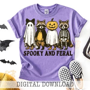 May include: A purple t-shirt featuring a Halloween design with four characters: a ghost, a raccoon, a pumpkin, and a skeleton raccoon. The text "Spooky and Feral" is printed below the characters. The words "Digital Download" are at the bottom.