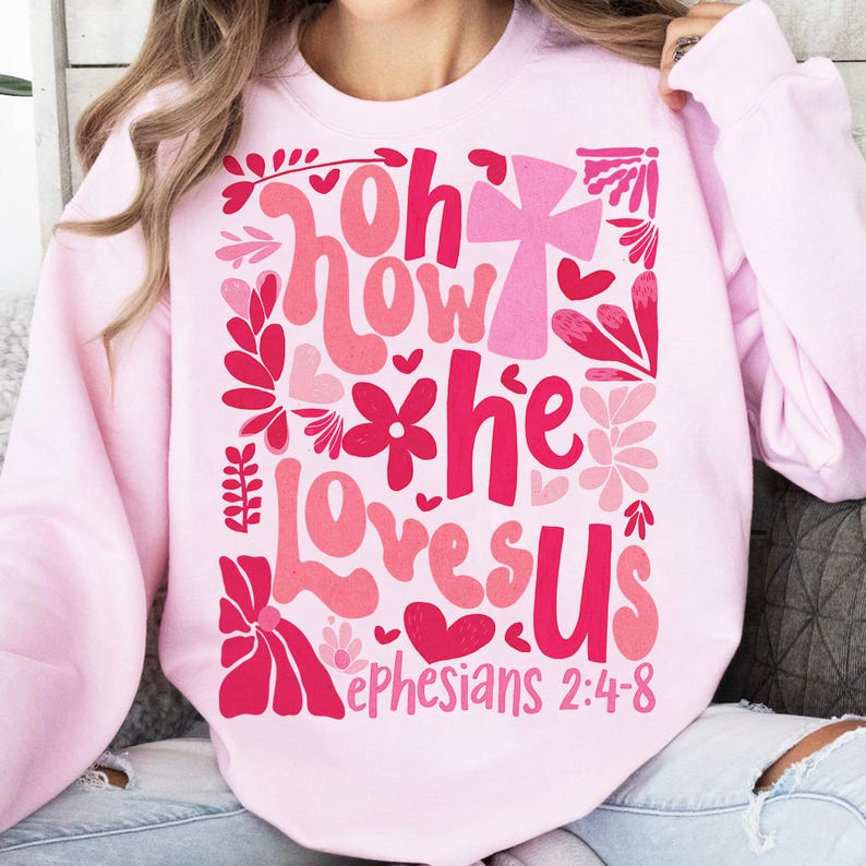 May include: Pink sweatshirt with a graphic design featuring a cross, flowers, and the text "Oh how he loves us Ephesians 2:4-8".