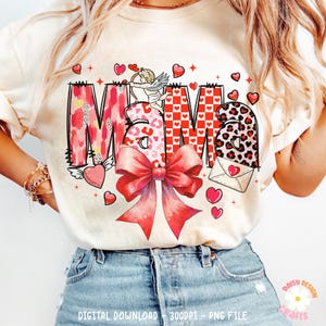 May include: A white t-shirt with a red, pink, and black graphic design that says "Mama" with a bow, hearts, and an angel with an arrow.