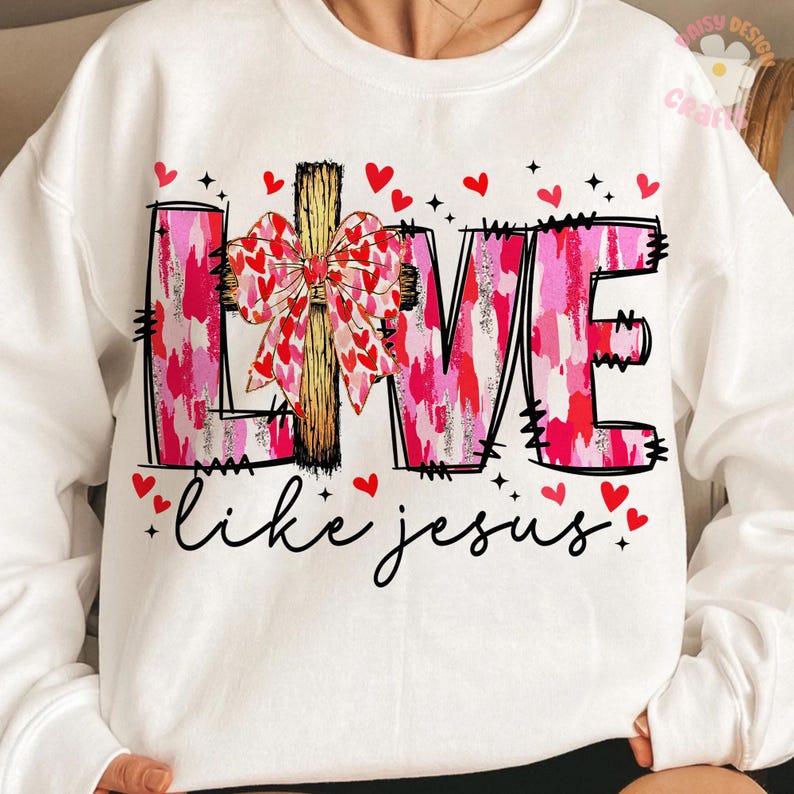 May include: White sweatshirt with the word "LOVE" in pink and red brushstroke letters, a wooden cross, and a bow made of hearts. The phrase "like jesus" is written in cursive below, with red hearts scattered around.