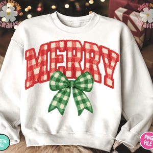 May include: White sweatshirt with the word "MERRY" in red and white plaid lettering. A green and white plaid bow is centered below the word. The sweatshirt is a festive holiday design.