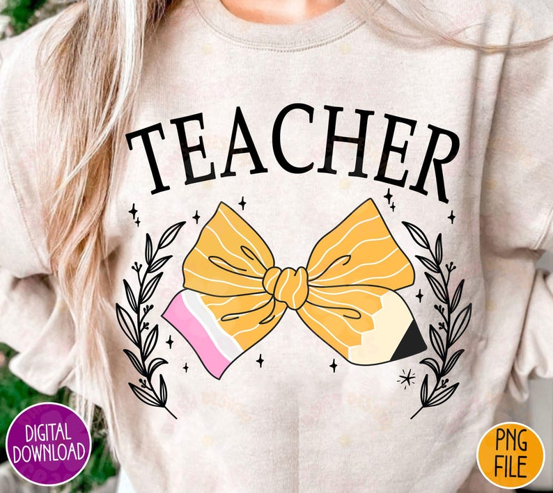 K&ouml;nnte beinhalten: Ein hellbeiger Pullover mit dem Wort "TEACHER" in Schwarz bedruckt. Eine gelbe Bleistiftschleife mit rosa und wei&szlig;en Akzenten ist mittig auf dem Pullover platziert. Die Schleife ist von schwarzen Blumenranken umgeben.