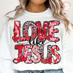 May include: White sweatshirt with a red, pink and black graphic print that says "Love like Jesus". The graphic features hearts, leopard print and glitter.