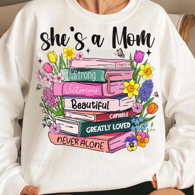 May include: White sweatshirt with the text "she's a Mom" in black script. A stack of books with words like "Strong" and "Beautiful" is surrounded by colorful flowers. A butterfly is also present in the design.